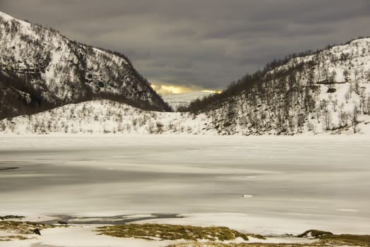 Winter landscape with snow, a frozen lake and a sunset far away