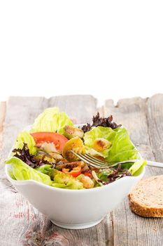 Healthy vegetarian salad with sauteed brussels sprouts in a mixed leafy green salad with tomato and radish served on an old grunge rustic wooden table, vertical orientation over white with copyspace