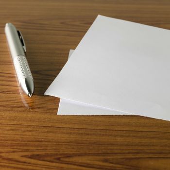 pen with white paper on wooden background