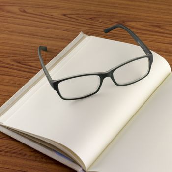 close up glass with notebook on wood background