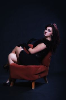 Young woman in retro clothes sitting on old orange chair