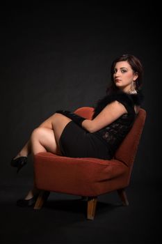 Young woman in retro clothes sitting on old orange chair