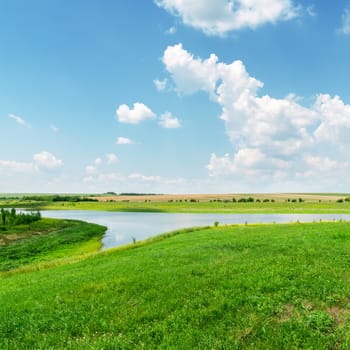 green grass, river and clouds in blue sky