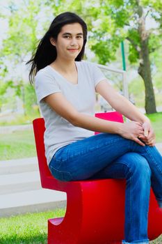 Beautiful biracial teen girl relaxing outdoors on red chair in summer
