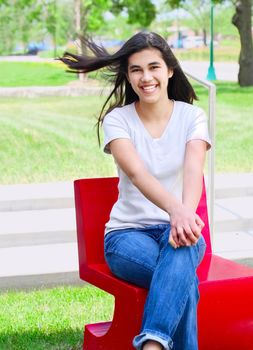 Beautiful biracial teen girl relaxing outdoors on red chair in summer