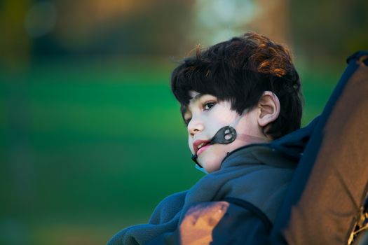 Handsome disabled boy sitting quietly in wheelchair at park, looking to side