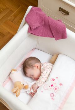 Portrait of cute baby girl sleeping in a cot with pacifier and stuffed toy