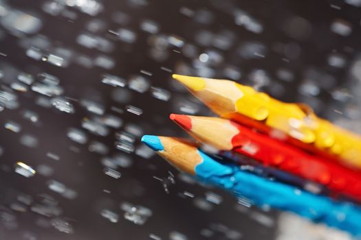 Three color pencils under the rain. Close-up view
