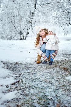 Young mother and daughter laughing for a walk in winter forest