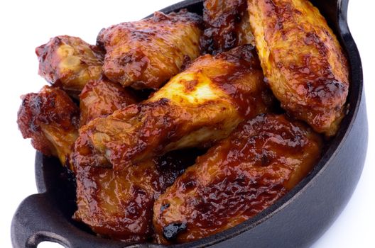 Hot Chicken Legs and Wings Barbecue in Black Saucepan closeup on White background