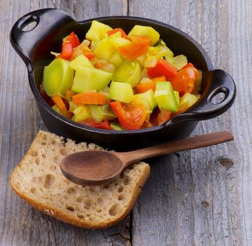 Vegetable Stew in Black Saucepan with Brown Bread and Wooden Spoon closeup on Rustic background