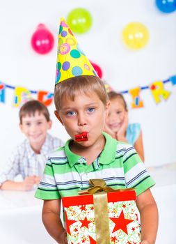 Handsome boy with giftbox looking at camera having fun at birthday party with his friends on background