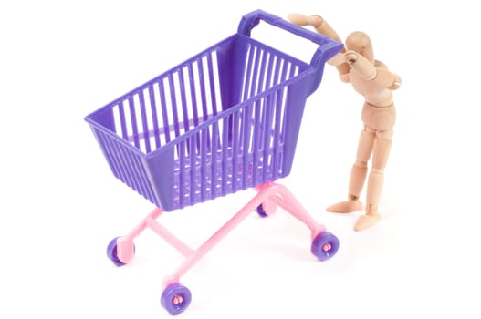 Conceptual photo with miniature shopping-cart and wooden man isolated on white