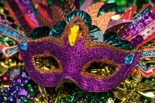 Close up view of purple sequined Mardi Gras mask with colorful beads out of focus in the background