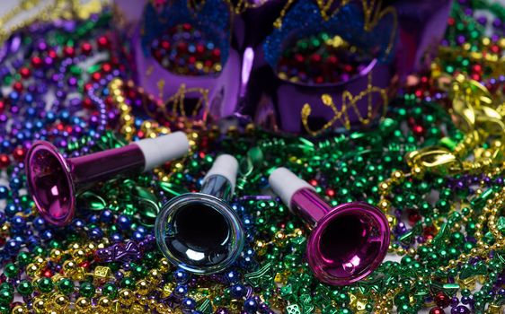 Mardi Gras celebration.  Purple Mardi Gras mask and horns on top of colorful beaded background