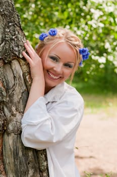 Smiling female in wreath from blue flowers near the tree