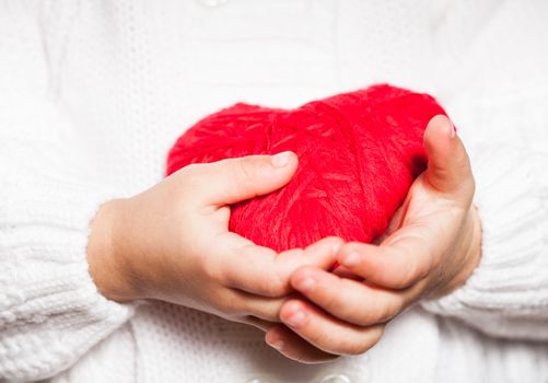 Red heart in hands of little kid in white blouse