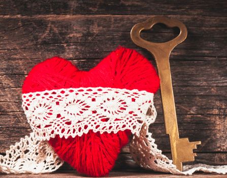 Red thread heart and golden key over wooden background