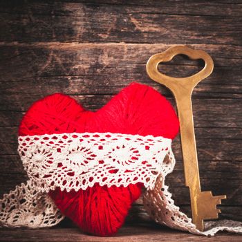 Red thread heart and golden key over wooden background