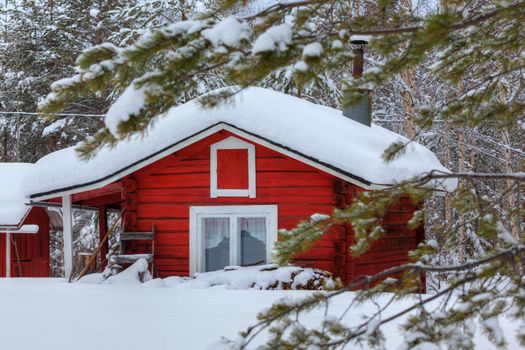 Red wooden Finnish house in winter forest covered with snow