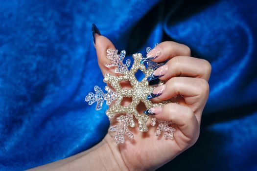 Female hand with beautiful manicure holding a snowflake shot closeup