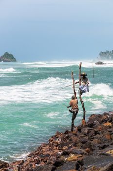 WELIGAMA, SRI LANKA - FEBRUARY 20: Asian men fishes in the traditional way while sitting on a pole on February 20, 2013 in Weligama, Sri Lanka. This type of fishing is traditional for south Sri Lanka and only one of this kind in the world.