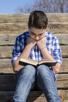 Outdoor.Young boy reading a book in the woods with shallow depth of field and copy space