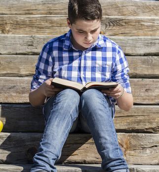 Young boy reading a book in the woods with shallow depth of field and copy space