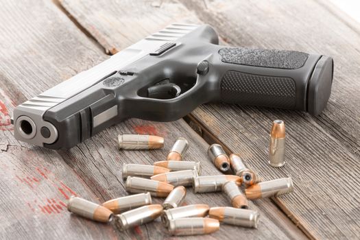 Handgun and a pile of scattered bullets lying on an old rustic wooden table conceptual of crime, violence, killing, coercion and protection of assets