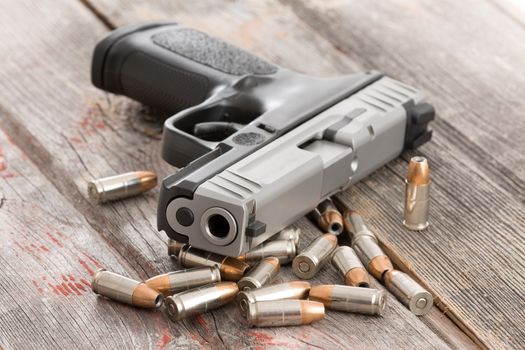 Looking up the muzzle of a handgun surrounded by scattered bullets and ammunition lying on old rustic wooden boards conceptual of violence, killing, crime and burglary