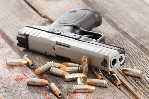 Close up view of the barrel of a handgun with scattered bullets and cartridges lying on old rustic wooden boards depicting violence, crime and robbery with copyspace