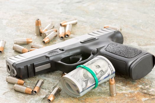 Conceptual image of a handgun with a roll of money surrounded by scattered bullets and cartridges on an old weathered wooden surface with copyspace depicting crime, a payoff, robbery or bribe