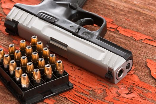 Close up of the barrel of a handgun and full rack of ammunition lying on a grungy wooden surface with red peeling paint conceptual of law enforcement, crime, violence and protection