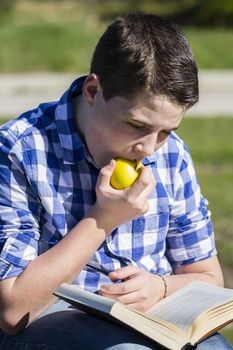 Eating.Young man reading a book in outdoor with yellow apple.