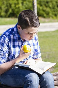 Happiness.Young man reading a book in outdoor with yellow apple.