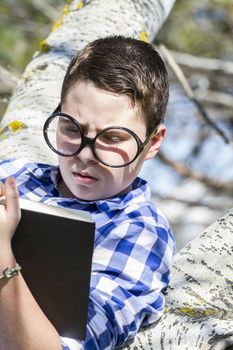 Think.Huge glasses.Student boy reading a book in the woods with shallow depth of field and copy space