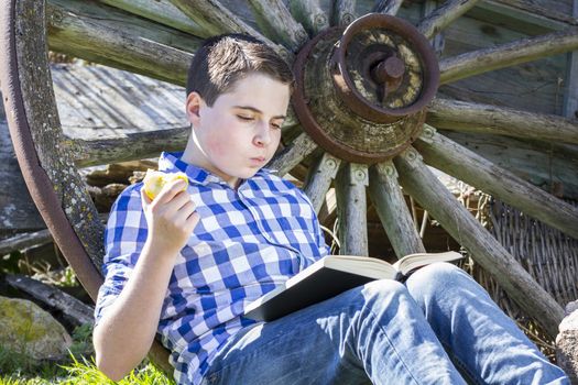 Young boy reading a book in the woods eating an apple