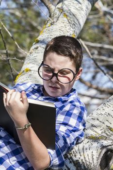 Funny.Huge glasses.Student boy reading a book in the woods with shallow depth of field and copy space