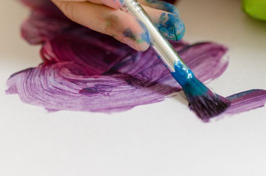 Child painting with an paint brush and water colors on paper