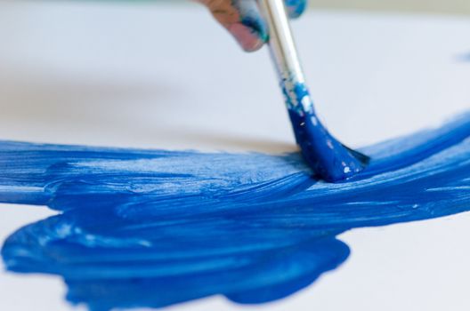 Child painting with an paint brush and water colors on paper