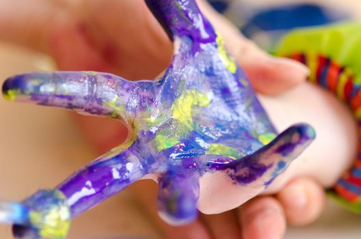 Child painting its hands in order to make a print on paper