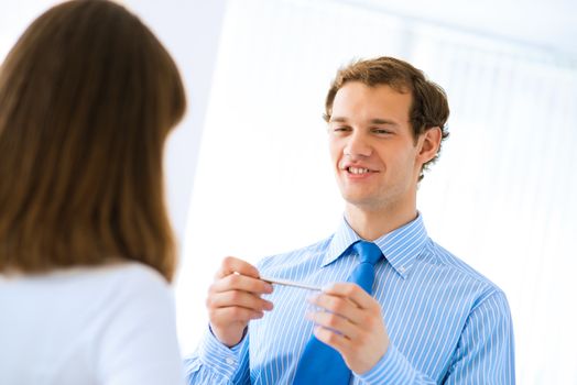 young businessman holds up a pen, talking with a colleague in front of