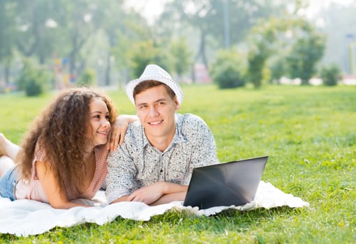 couple lying together in a park, working together on a laptop