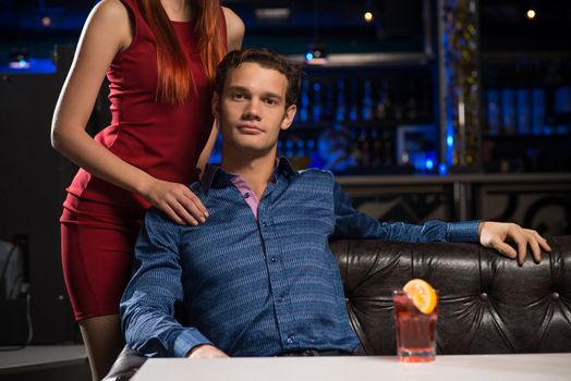 Portrait of a successful man in a nightclub, sitting on the couch, next to a woman in a red dress