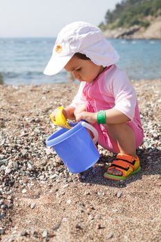 Baby play on seashore with rebbles and pail