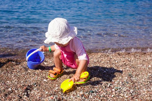 Baby play on seashore with rebbles and pail