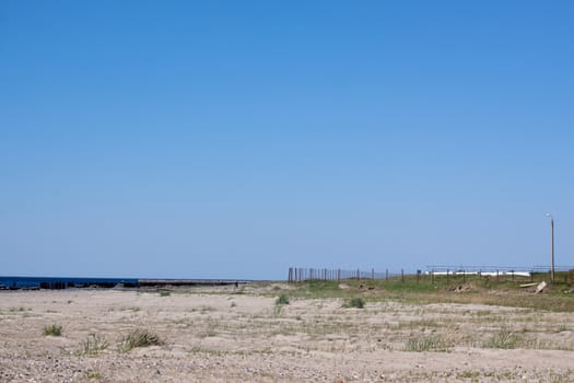 A landscape with sea, sand, fence and sky in sunny day
