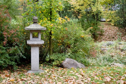 Bushes, stone traditional lamp and brown autumn leaves in a park 

