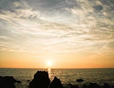 Sunset with clouds ocean and big rocks