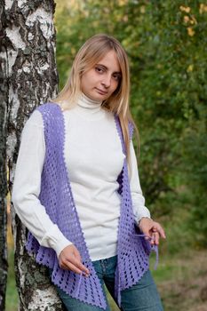 A girl in a lilac vest and white polo-neck sweater and jeans in a forest
